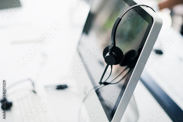 Fototapeta Computers desktop and headsets for communication and work from home.  Operator call center service help computer deck of worker.