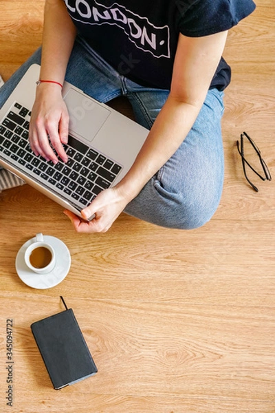 Fototapeta a girl sits on the floor with a laptop, near are glasses and a notebook for notes