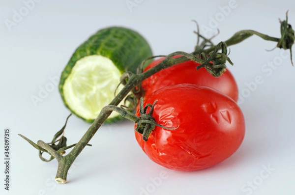 Obraz Wrinkled tomatoes and a half of cucumber lie on a table. Light gray background. Soft shadows. Selective focus.