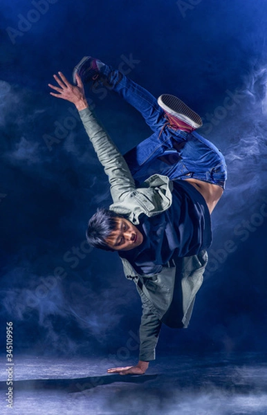 Obraz A street dancer stands on one hand against a dark background in a cloud of smoke