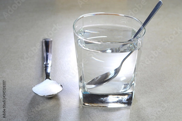 Obraz Salt water in a glass cup and salt in a teaspoon. Salt water has high level of minerals and salt water gargle helps in removing of cold and sore throat.