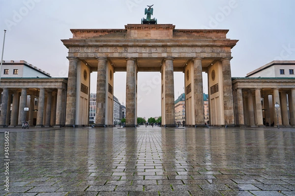 Fototapeta berlin germany, deserted brandenburg gate with reflections on the wet asphalt and with clouds. special perspective as close-up from the ground, tv tower and town hall in the background