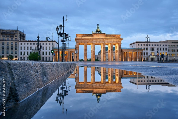 Fototapeta incredible view of the Berlin Brandenburg gate after the rain, reflection of the yellow gate in the water of a street puddle, blue skay with clouds in the background 