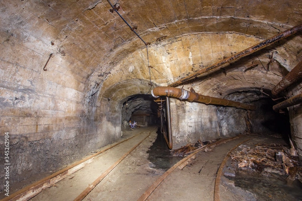 Fototapeta Underground abandoned iron ore mine tunnel with concrete timbering and rails
