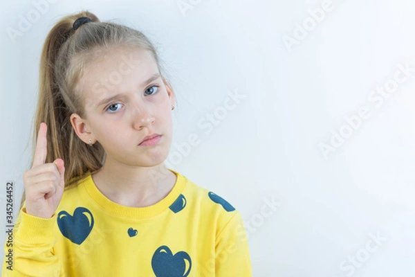 Fototapeta Vivid or colorful workpiece with funny, cool, pretty and nice girl in yellow sweater or tee-shirt on white background for easy extraction holding her forefinger up as attention or mentoring sign