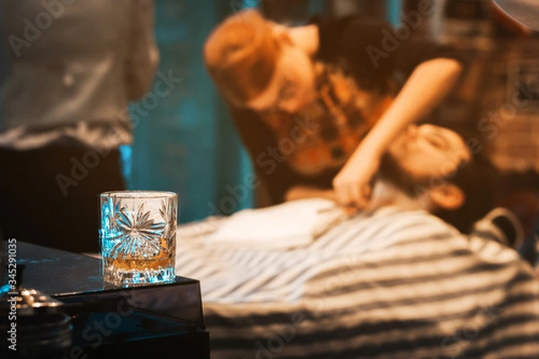 Fototapeta Whisky glass with client getting shave in barbershop in background