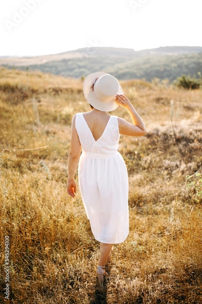 Fototapeta Beautiful girl with hat walks in the mountains and enjoys the sunset. Back view