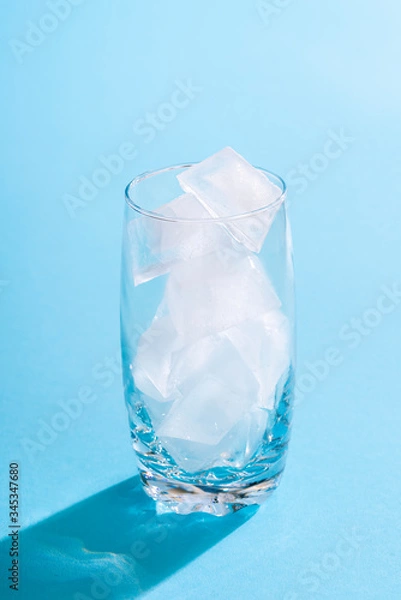 Fototapeta Glass with ice cubes on blue background. Empty glass with ice