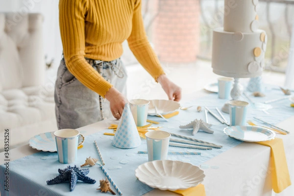 Obraz Woman serving party table in blue colors with textile tablecloth, white dishes, glasses for wine and golden cutlery. Happy birthday decoration.