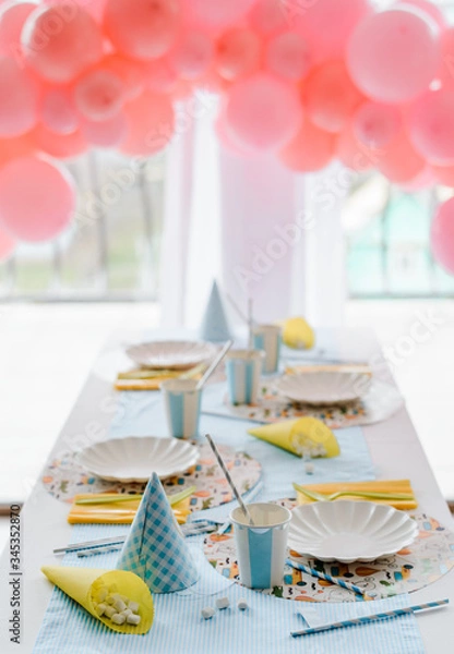 Fototapeta Decorative festive table setting for kids party dinner with textile napkin and tablecloth in sky blue and yellow colors . Pink balloons decoration
