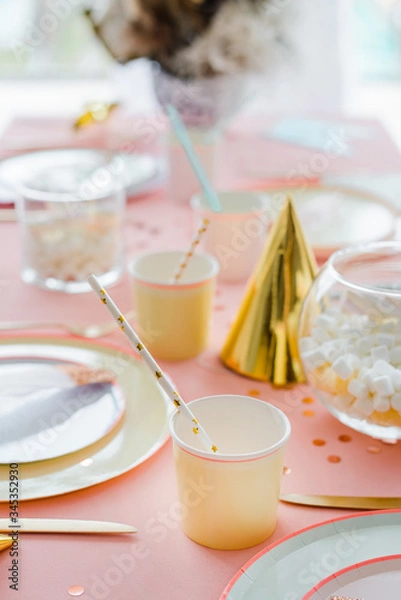 Fototapeta Decorative festive table setting for kids party dinner with textile pink tablecloth, paper colorful cups and plates with cocktail straws. Happy birthday decoration