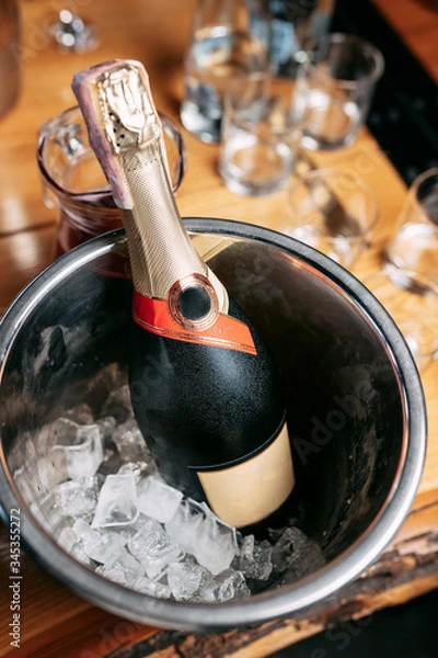 Fototapeta a bottle of champagne in a bucket with ice on the background of a wooden table