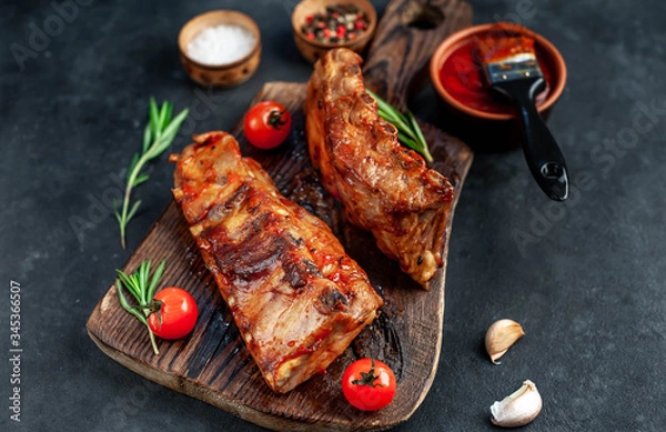 Fototapeta Grilled pork ribs with spices on a cutting board on a stone background
