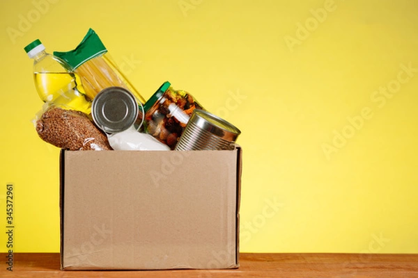 Fototapeta A box of food on the table. Humanitarian assistance to people in difficult situations due to the COVID 19 coronavirus pandemic. Volunteer package for the elderly.
