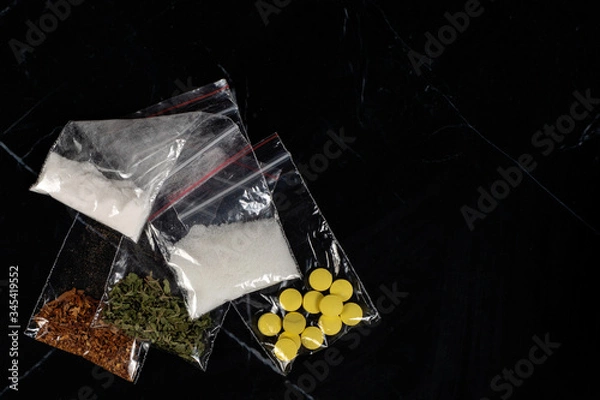 Fototapeta lethal concept: tobacco, weed, MDMA tablets, amphetamine crystals, heroin in plastic bags, on a dark background. Enhanced contrast, partial blur.