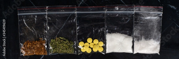 Fototapeta lethal concept: tobacco, weed, MDMA tablets, amphetamine crystals, heroin in plastic bags, on a dark background. Enhanced contrast, partial blur.