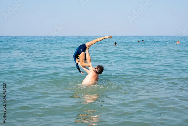 Fototapeta Father, playing with child at the seaside. Executing water jumps.