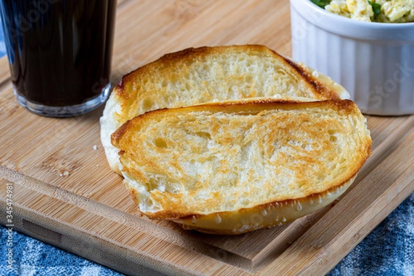 Obraz traditional Brazilian breakfast. Coffee in a glass, toasted bread and butter, and scrambled eggs, on top of a wooden board and a blue cloth (Pão na Chapa)