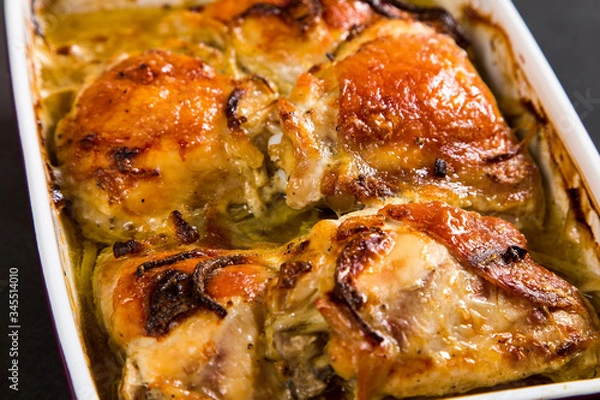 Fototapeta Baked chicken thighs with onions in ceramic form on a stone table, copy space.