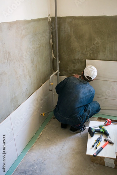 Fototapeta Worker installing big ceramic tiles on the walls