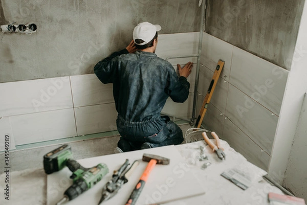 Fototapeta Worker repairman puts large ceramic tiles on the walls in the room