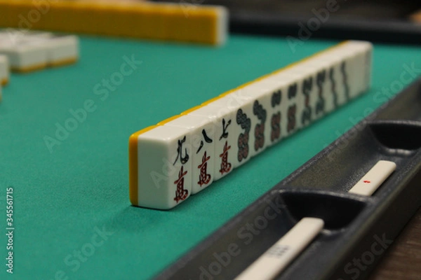 Obraz The bones (tiles) for the mahjong lie on the green table, the back and side plan is blurred. Table traditional game of Asia.