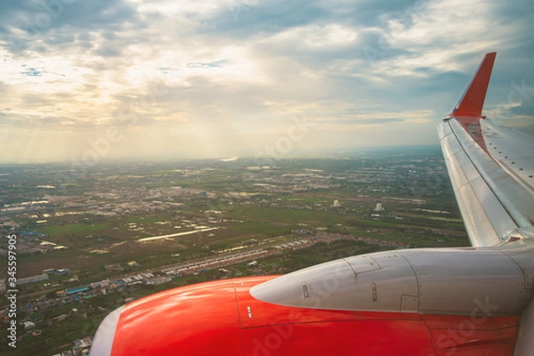 Fototapeta Beautiful scenic city view of sunset through the aircraft window..Airplane interior with window view of blue sky and wing..Looking through window aircraft during flight in wing with a nice blue sky.