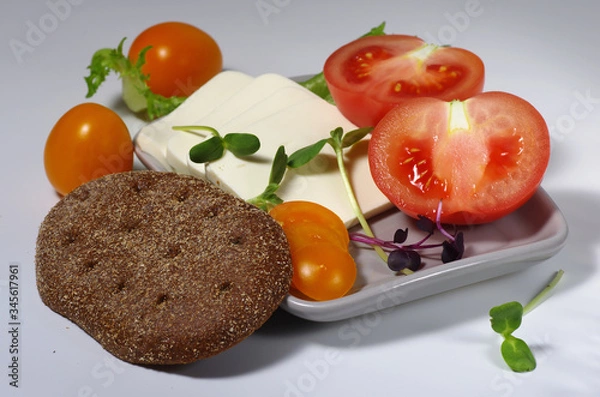 Obraz Sliced pink and yellow tomatoes and feta cheese on a plate with a piece of brown bread. Gray background. Selective focus.