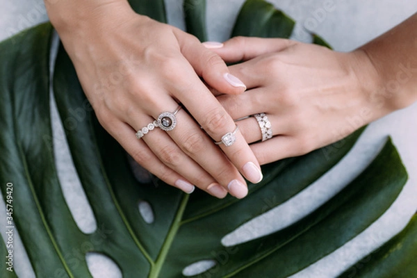 Obraz jewelry made of gold and diamonds on the girl’s hands on the background of a large green leaf of monstera