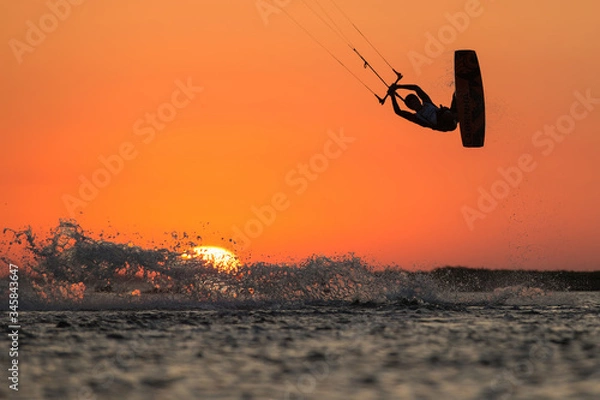 Fototapeta Professional kiter rides in the ocean against the background of incredible setting sun