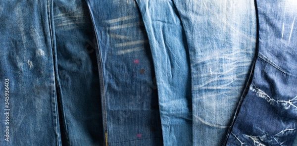 Fototapeta Stack of various shades blue jeans. Jeans stacked isolated on white background. Blue denim jeans texture banner with copy space for text design background. Canvas denim fashion texture