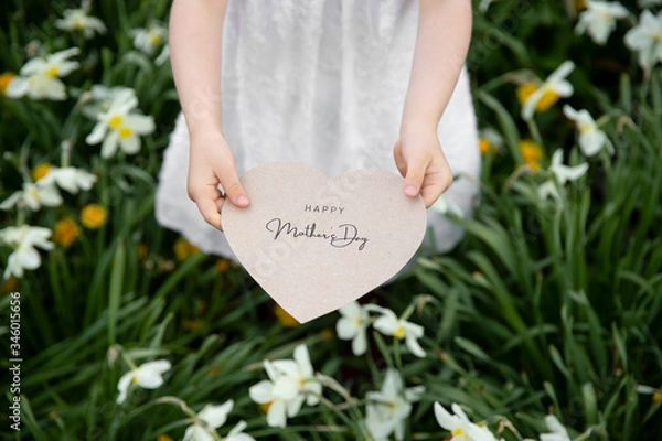 Obraz Happy Mother's Day written on a paper card held by a girl on a flower and grass background