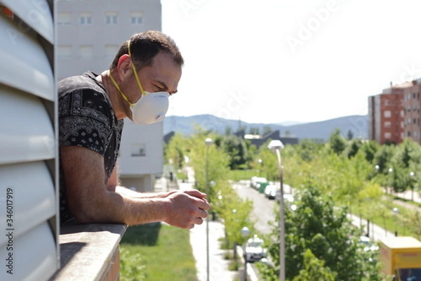 Obraz middle age man in mask staying at home, look from the balcony 