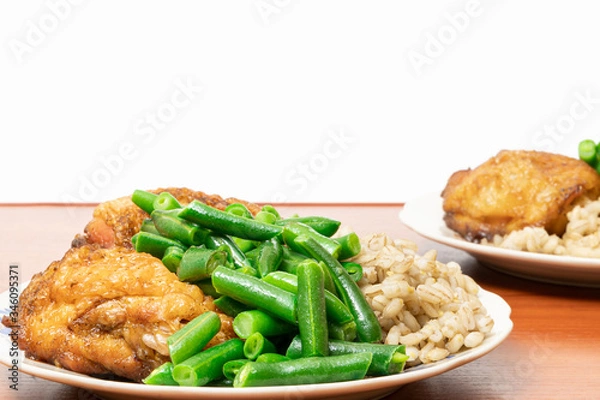 Fototapeta green asparagus beans on a plate with golden chicken thighs and pearl barley porridge on a table on a white background. healthy diet food.