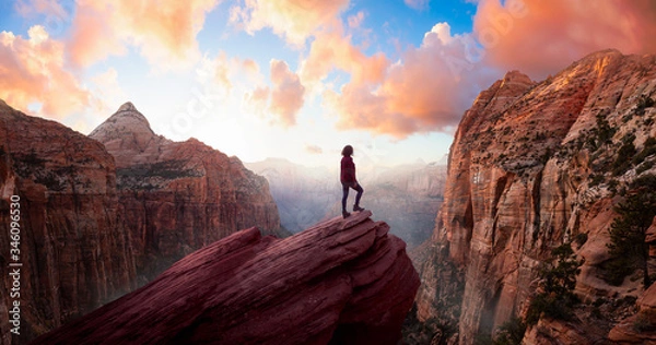 Obraz Przygodowa kobieta na skraju klifu patrzy na piękny widok krajobrazu w kanionie podczas żywego zachodu słońca. Zrobione w Zion National Park, Utah, Stany Zjednoczone. Sky Composite Panorama