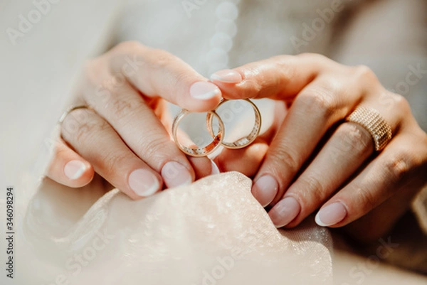 Fototapeta two golden rings in the hands of the bride that lie on a wedding white veil with a blurred background