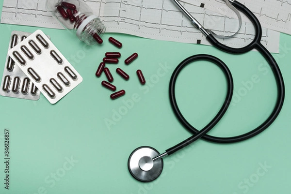 Obraz Stethoscope on an EKG with capsules on a green background. Electrocardiogram with black stethoscope
