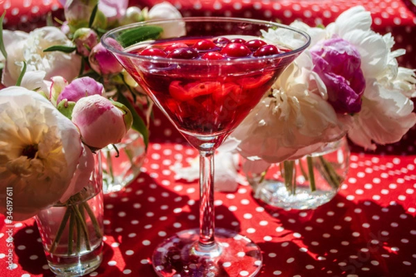 Fototapeta Magic solemn still life with glass of red drink with autumn organic berries surrounded by white flowers in the diagonal striped shadow of the blinds on a bright sunny day. Greeting card on textile