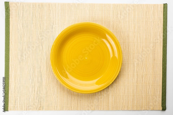 Obraz Empty Yellow plate on a bamboo napkin,top view
