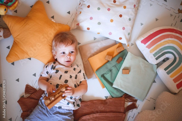 Obraz Happy baby boy playing with a wooden toy car lying on the floor