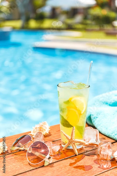 Fototapeta Glass of cclassic mojito cocktail and caipirinha with shells, sunglasses and blue towel closed to swimming pool. Vacation, summer, holiday, luxury resort concept.