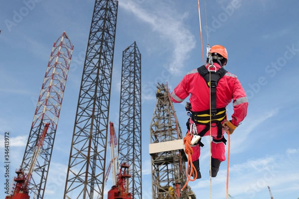 Obraz Industrial rope access abseiler welder wearing safety harness, abseiling commencing on structure steel of rig drilling background