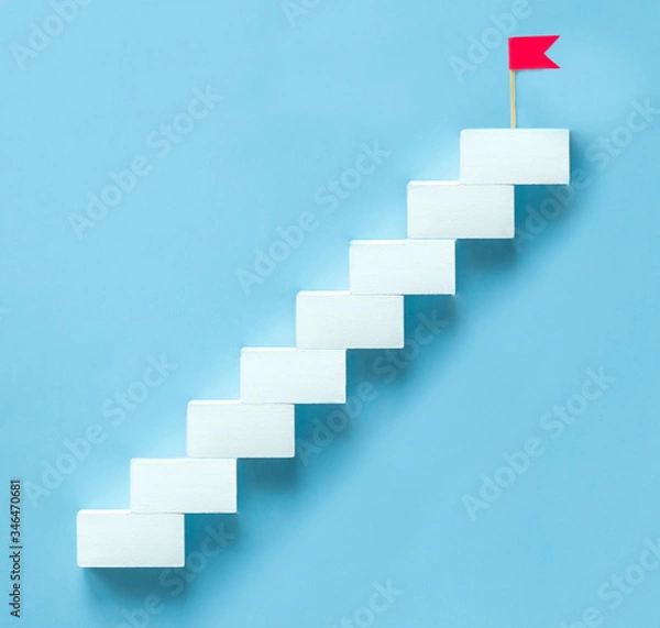 Fototapeta Concept to achieve the goal, the upward movement. White staircase with a red flag on the top step on a blue background