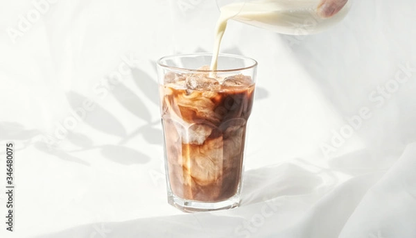 Obraz Milk cream is poured into a iced coffee cold brew.  Coffee cold drink with ice and milk.