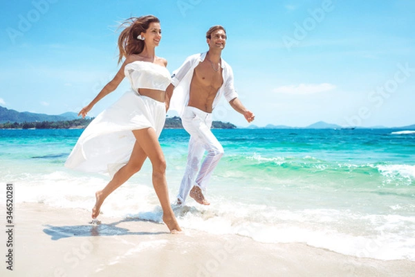 Fototapeta A couple in white clothes is resting on the beach of a wonderful island. Paradise weekend