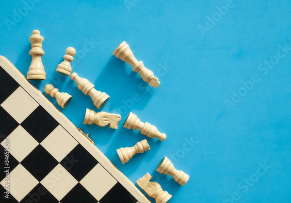 Obraz White chess pieces lying next to a chessboard, top view.