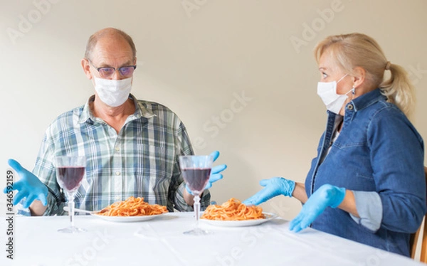 Fototapeta Senior couple looking surprised to their dinner, they are wearing white medical protective masks - coronavirus protection measures concept (at restaurant and bars)