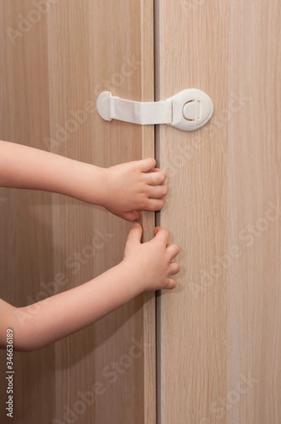 Fototapeta Hands of a little kid pulling the closet door closed with a special lock for child safety