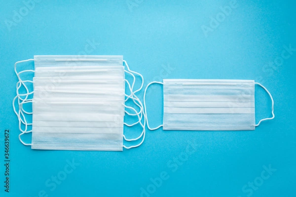 Fototapeta White protective medical masks on a blue background, several in a row on the left,one on the right