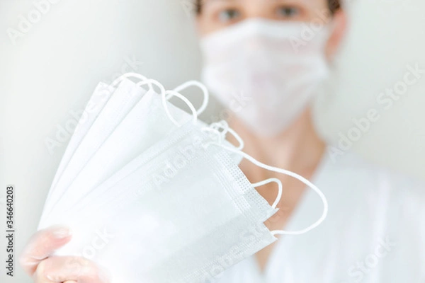 Fototapeta White protective medical masks in hand in the foreground ,a woman with a mask in the background in the center.